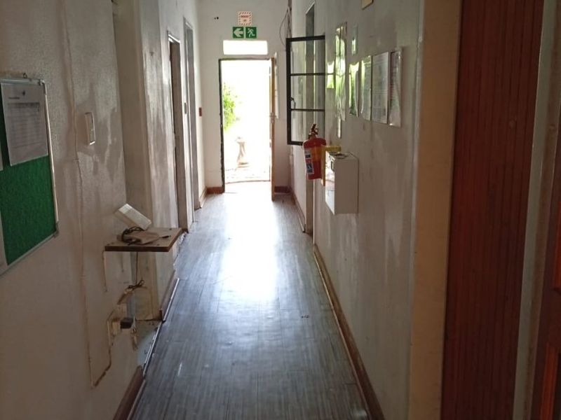 A long hallway featuring pressed metal ceilings, laminate flooring, and multiple timber doors leading to adjacent rooms, with visible wear on the wall finishes.