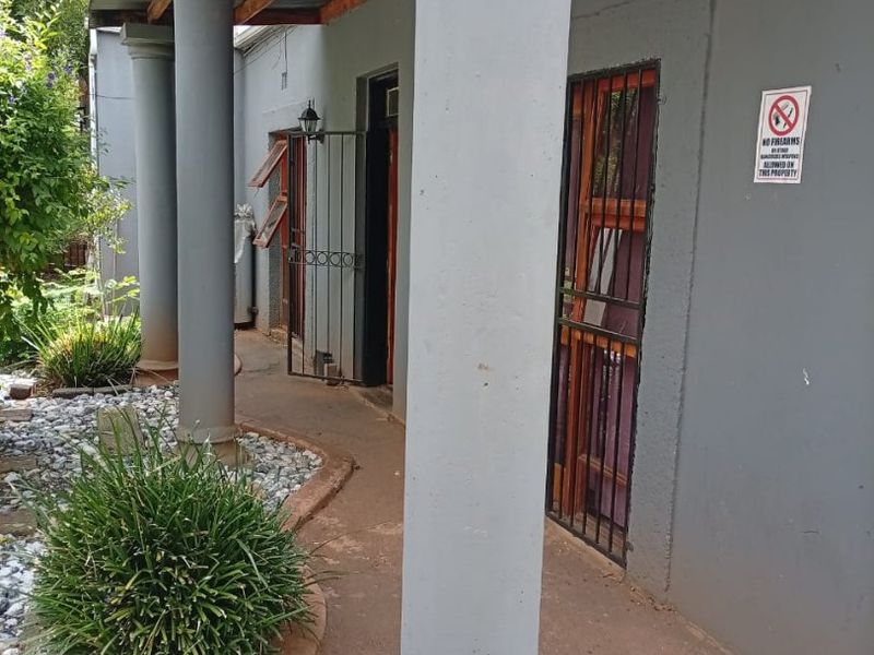 A covered patio area featuring concrete columns, a corrugated metal roof, and security gates, providing access to the building's exterior.