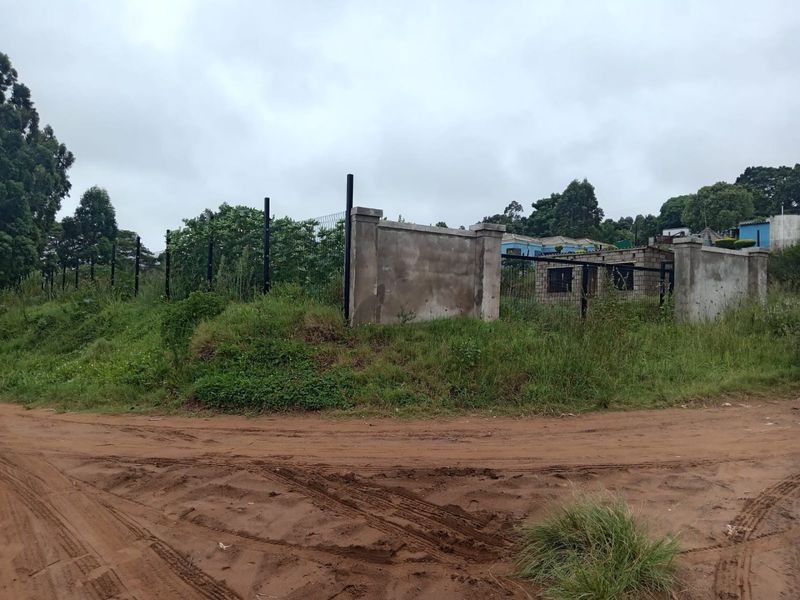 A view of a vacant residential plot featuring perimeter fencing and an unfinished concrete boundary wall, accessible via an unpaved road.