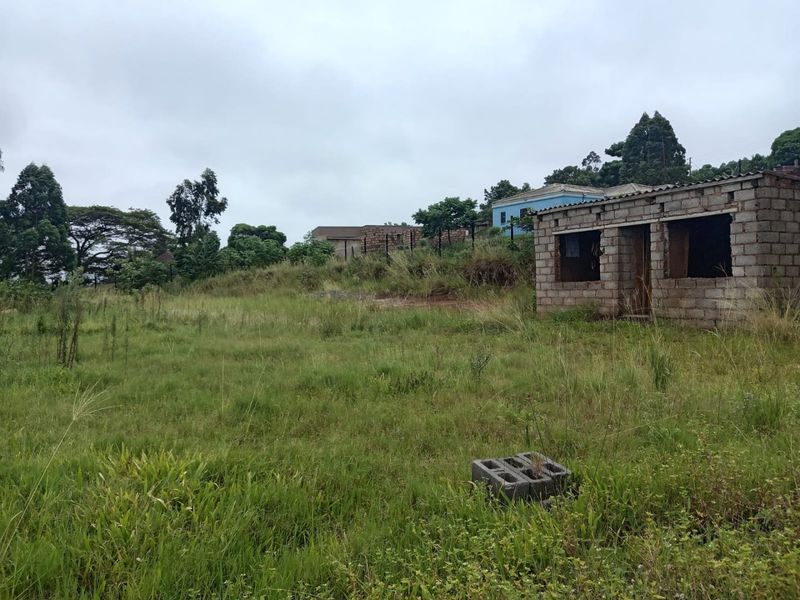 A vacant residential plot featuring an unfinished concrete block structure and overgrown grass, offering potential for development.