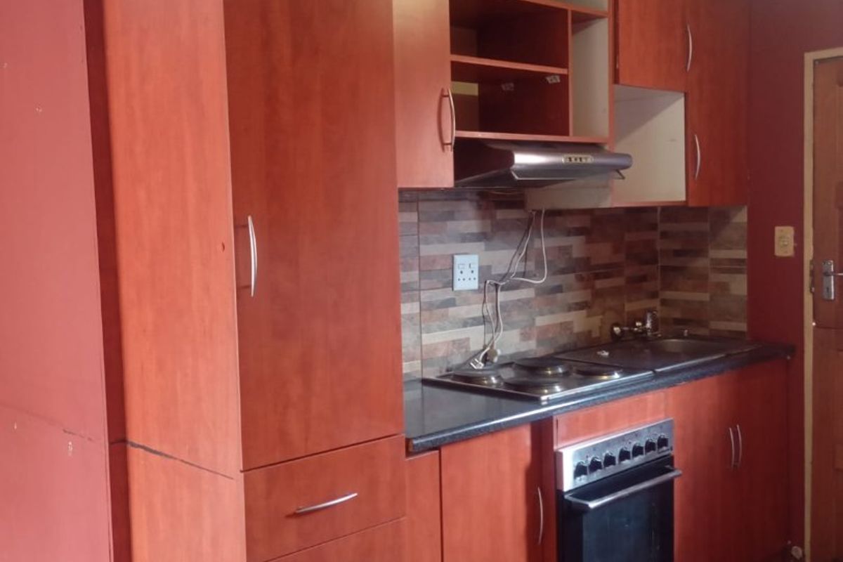 A compact kitchen featuring built-in cabinetry, an electric hob, oven, and tiled splashback. The space requires cosmetic updates to the ceiling and finishes.