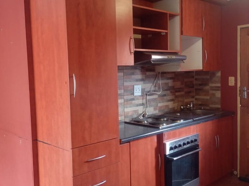 A compact kitchen featuring built-in cabinetry, an electric hob, oven, and tiled splashback. The space requires cosmetic updates to the ceiling and finishes.
