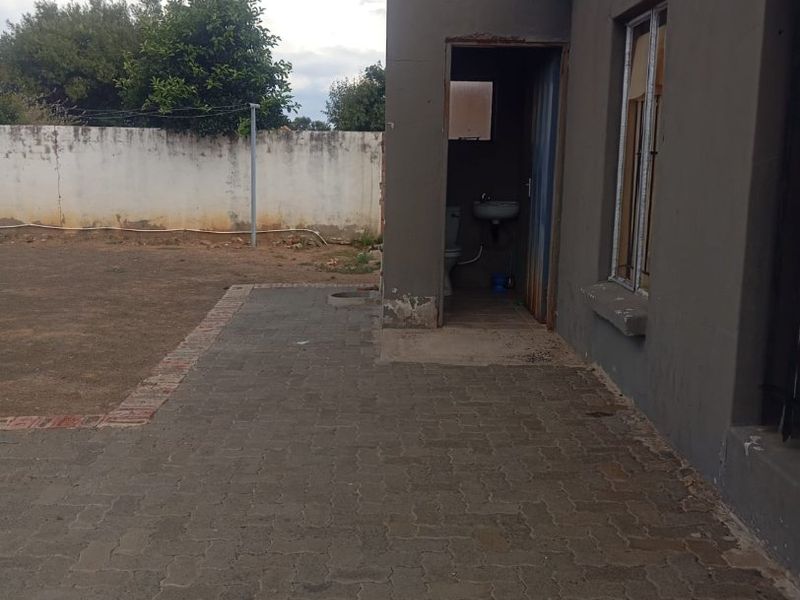 Rear exterior view showing a paved patio area, boundary wall, and access to an external toilet facility with a washbasin.