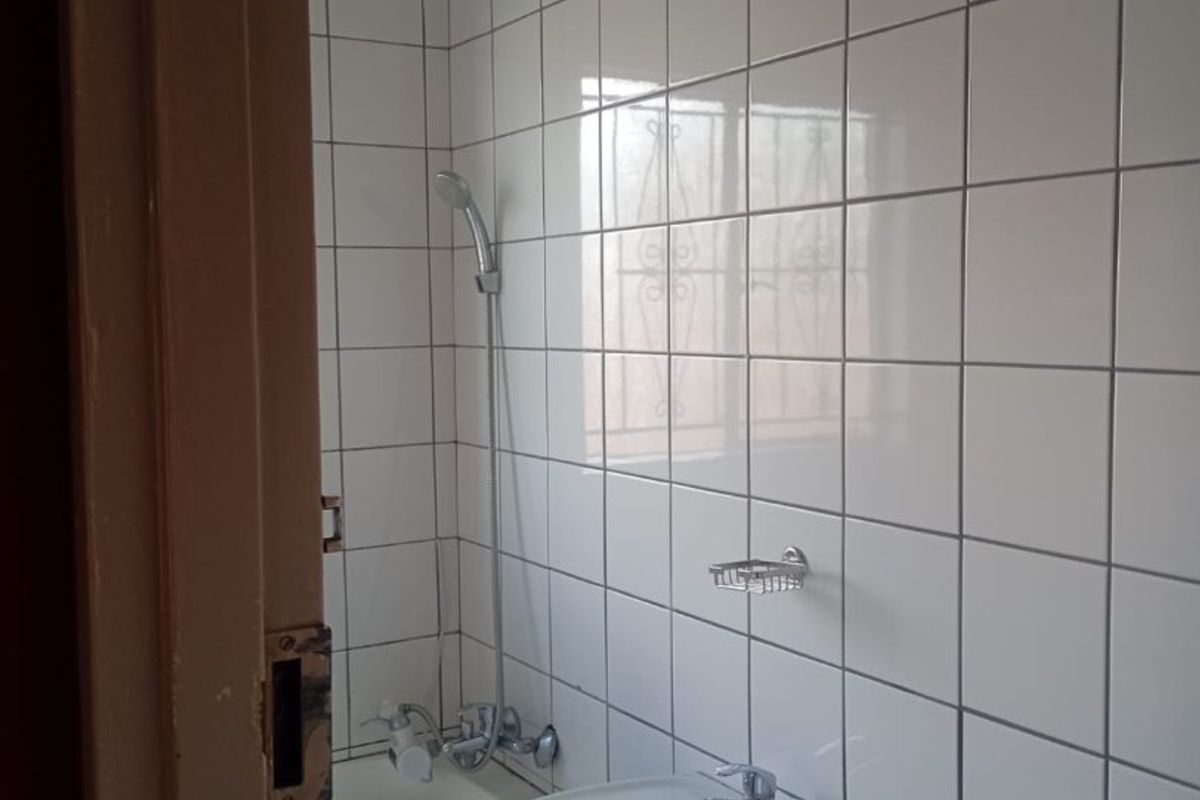 A compact bathroom featuring white ceramic wall tiles, a pedestal basin, and a built-in bathtub with a handheld shower attachment.