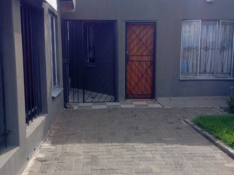 Rear exterior view of the property featuring a paved courtyard area, security gates, and metal security bars on windows.