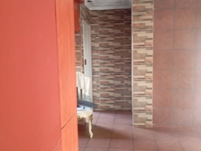 A hallway area featuring ceramic floor tiles and decorative stone-look wall cladding, presenting a dated aesthetic in need of modernization.