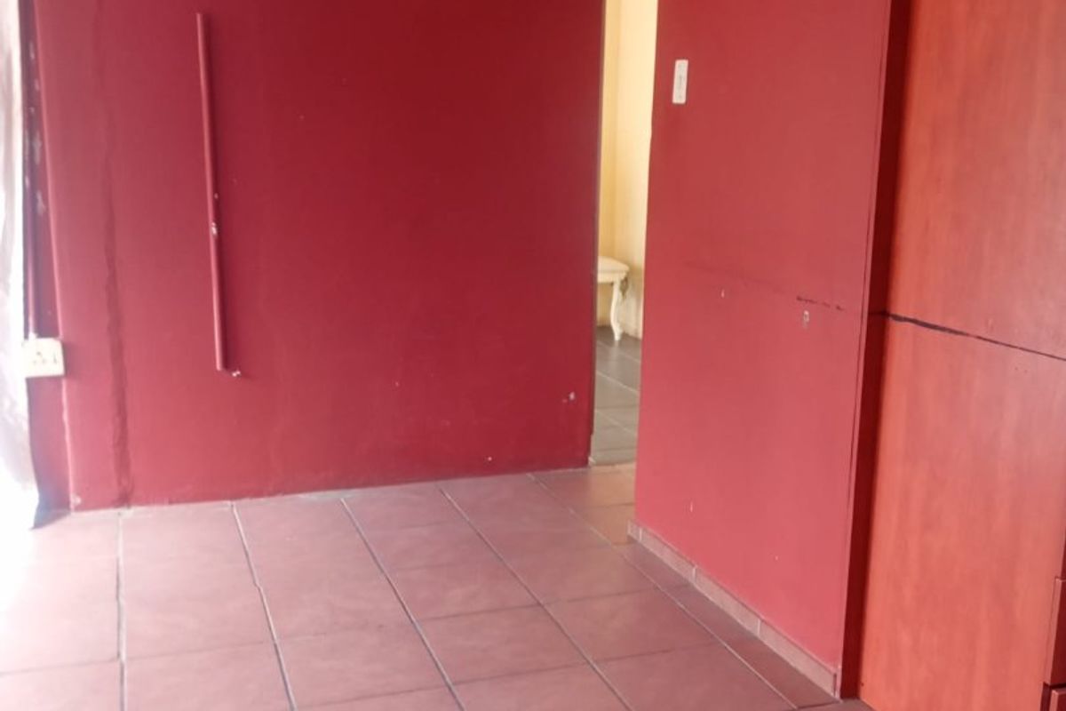 An empty bedroom featuring tiled flooring and a built-in wardrobe, requiring cosmetic updates to the wall finishes.