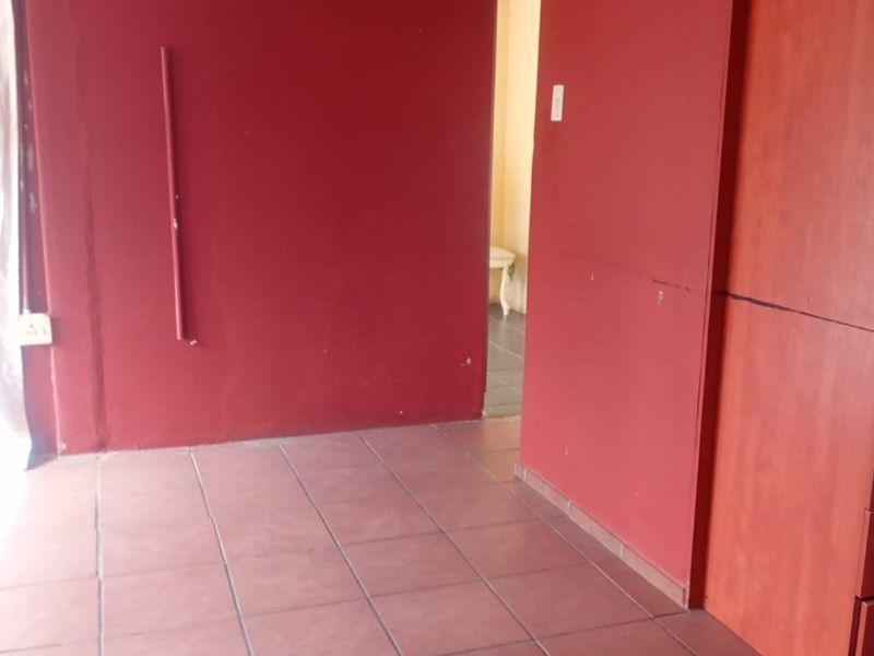 An empty bedroom featuring tiled flooring and a built-in wardrobe, requiring cosmetic updates to the wall finishes.