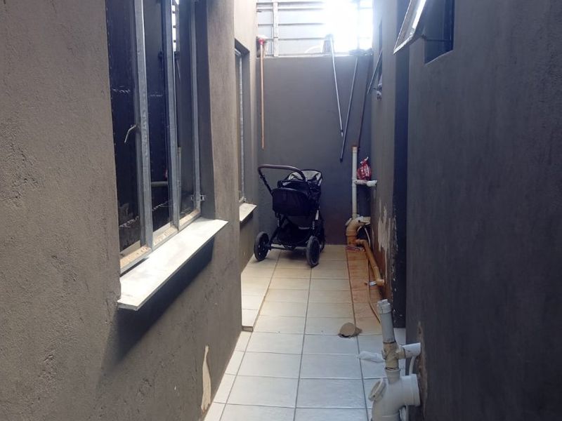 A narrow exterior side passage featuring tiled flooring, exposed plumbing, and painted masonry walls.