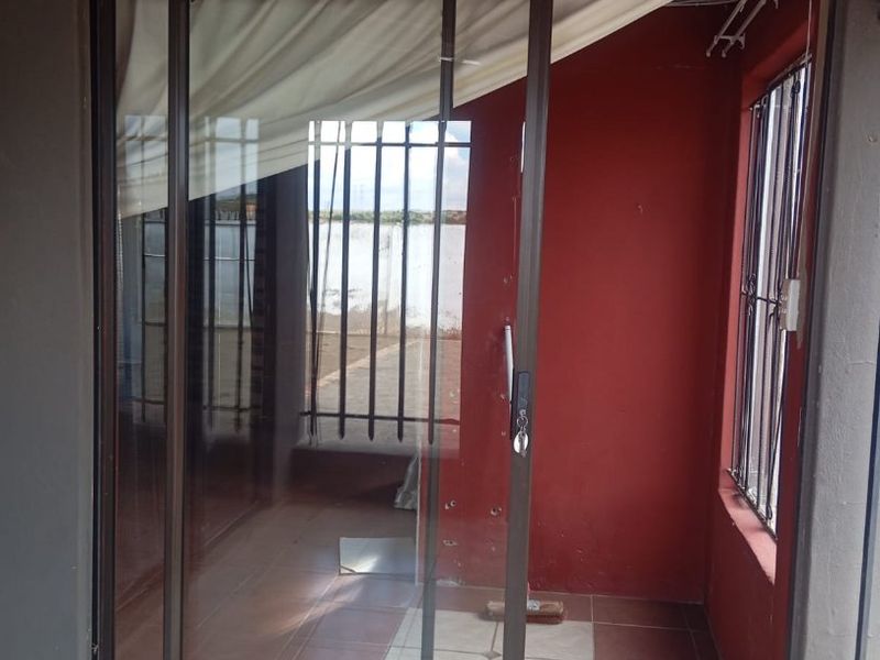 A covered patio area featuring tiled flooring, sliding glass doors, and security bars, currently requiring cosmetic updates to the walls and ceiling.