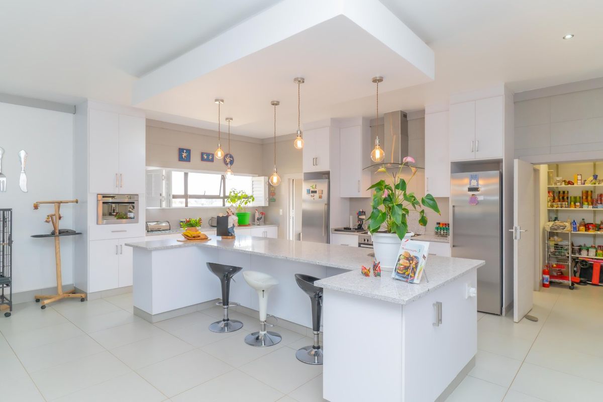 Modern kitchen featuring a large island with granite countertops, built-in appliances, pendant lighting, and an adjacent walk-in scullery.