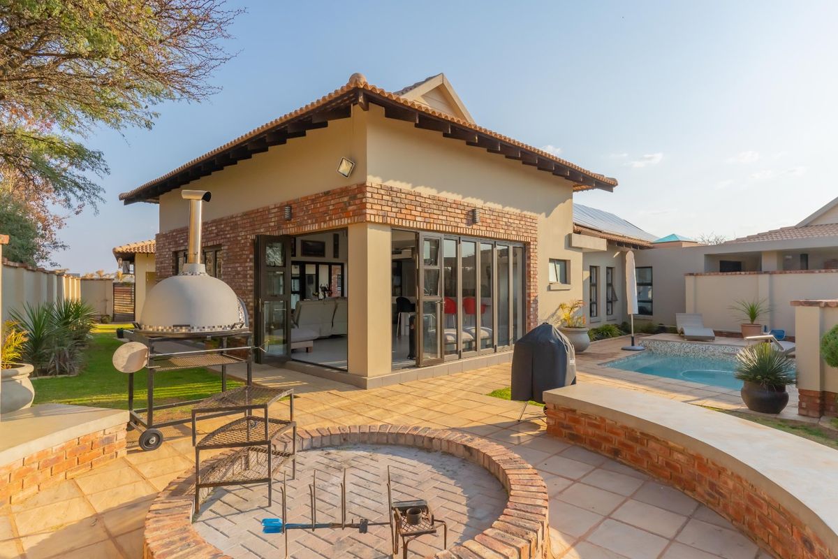 Rear exterior view featuring a tiled patio, built-in brick fire pit, swimming pool, and bi-fold doors leading into the living area.