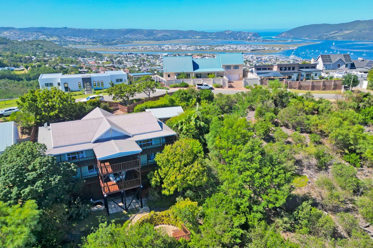 Aerial view of a multi-level residential property featuring a metal roof, timber decking, and elevated stilt construction, set within a lush, established garden.