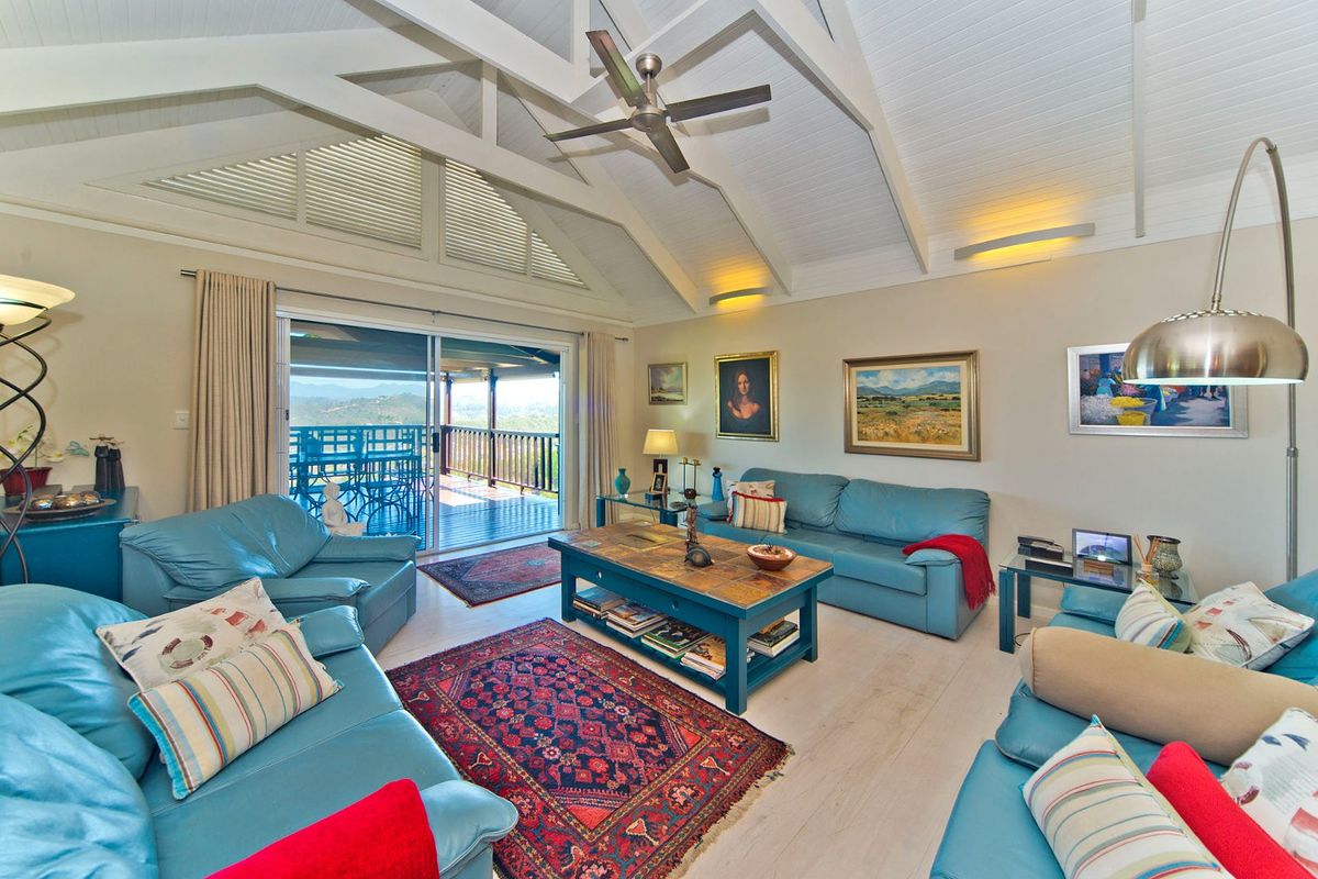 Spacious living room featuring a high vaulted ceiling with exposed beams, ceiling fan, and large sliding glass doors leading to an outdoor deck.