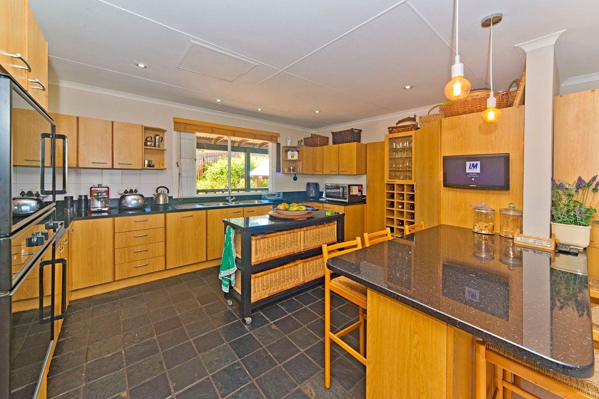 A functional kitchen featuring light wood cabinetry, dark granite countertops, slate flooring, and a built-in double oven with ample storage space.