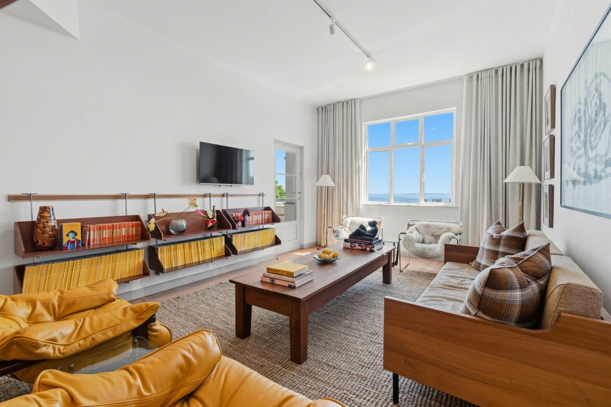 A bright and well-maintained living room featuring track lighting, large windows with curtain tracks, and a wall-mounted television setup.