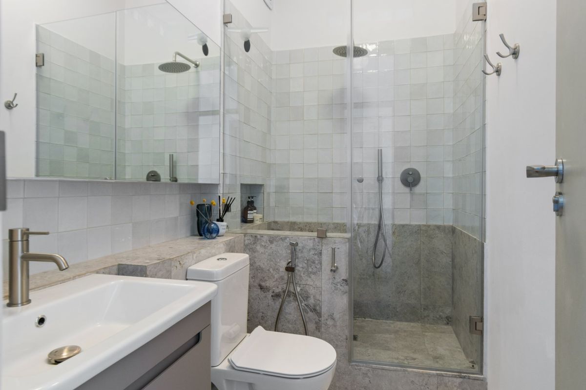 Modern bathroom featuring a walk-in shower with glass screen, stone vanity countertop, and built-in mirror cabinetry with high-quality tiled finishes.