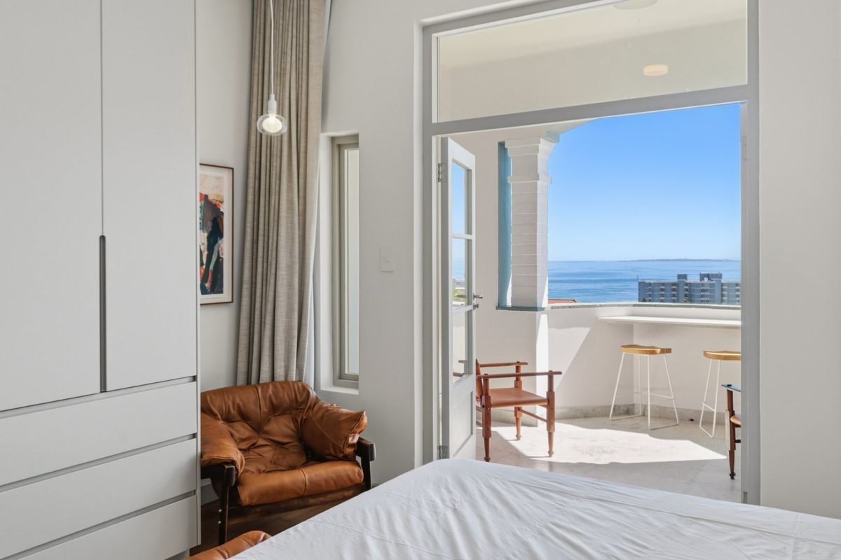 A bright bedroom featuring built-in wardrobes and direct access to a private balcony with stunning ocean views.