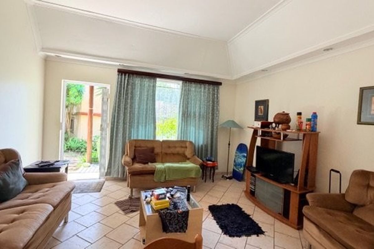 Spacious living room featuring vaulted ceilings, ceramic tile flooring, and direct access to the outdoor area through a sliding glass door.