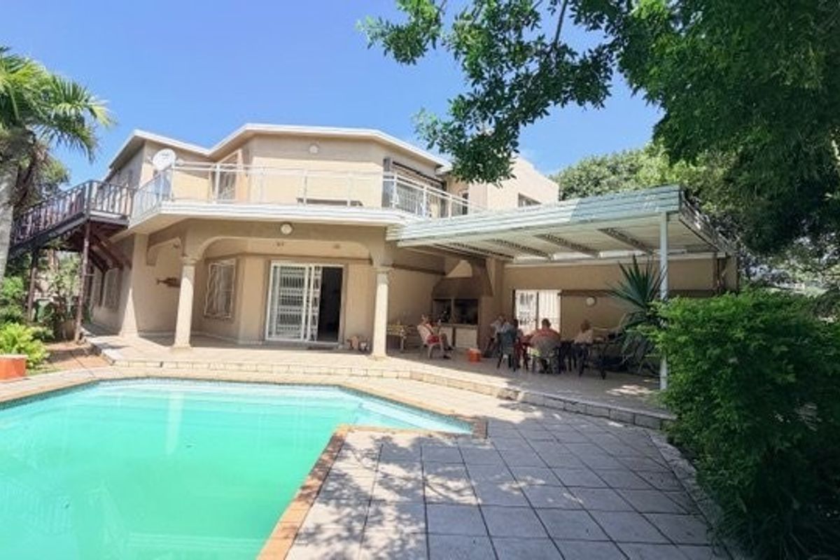 Rear view of the property featuring a swimming pool, paved patio area, built-in braai, and an upper-level balcony.