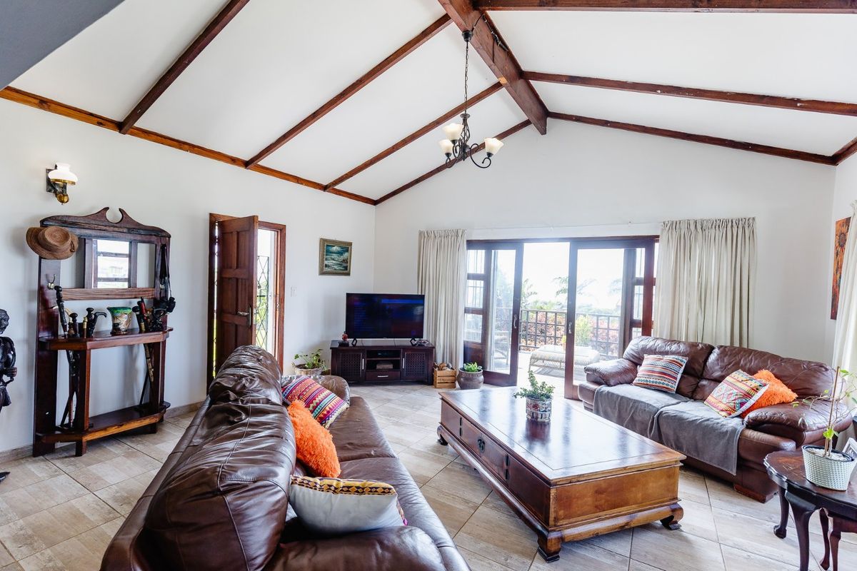 Spacious living room featuring a vaulted ceiling with exposed timber beams, tiled flooring, and double glass doors leading to an outdoor area.