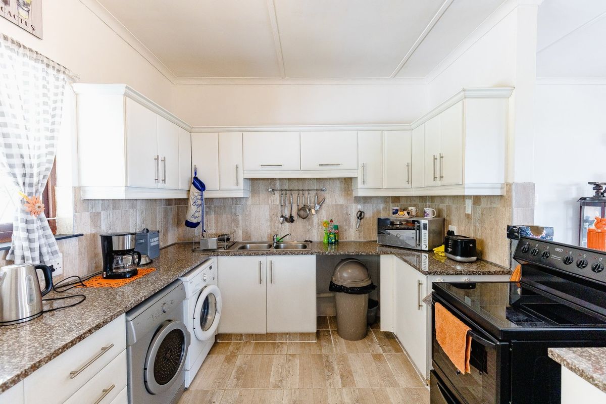A functional kitchen featuring white cabinetry, granite countertops, tiled backsplash, and integrated laundry appliances, offering a practical layout for daily use.
