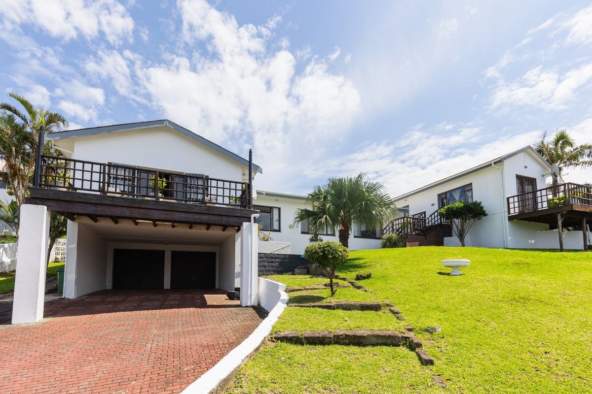 Rear view of the property featuring a double garage, raised timber deck, brick paved driveway, and a landscaped garden with stone steps.