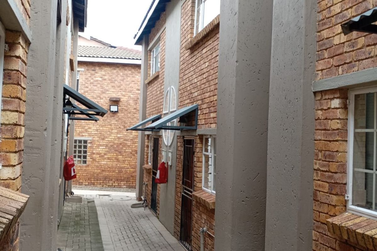 A narrow exterior walkway between apartment blocks featuring face-brick walls, paved flooring, and external water taps.