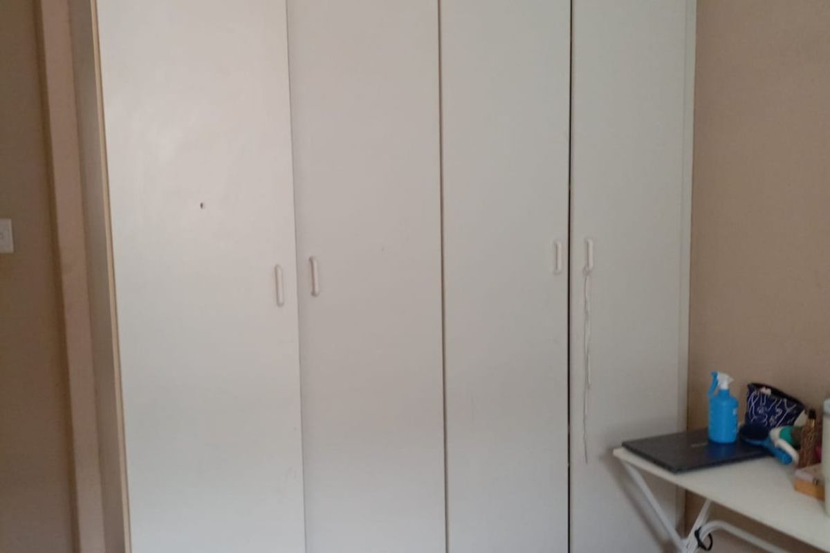 A bedroom featuring a large, built-in white wardrobe with four doors, providing ample storage space.