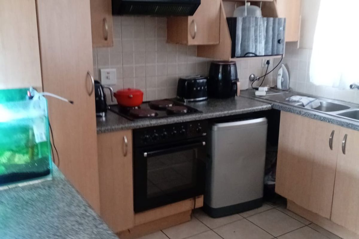 A functional kitchen featuring light wood cabinetry, granite-look countertops, a built-in oven, hob, and extractor fan with tiled flooring.