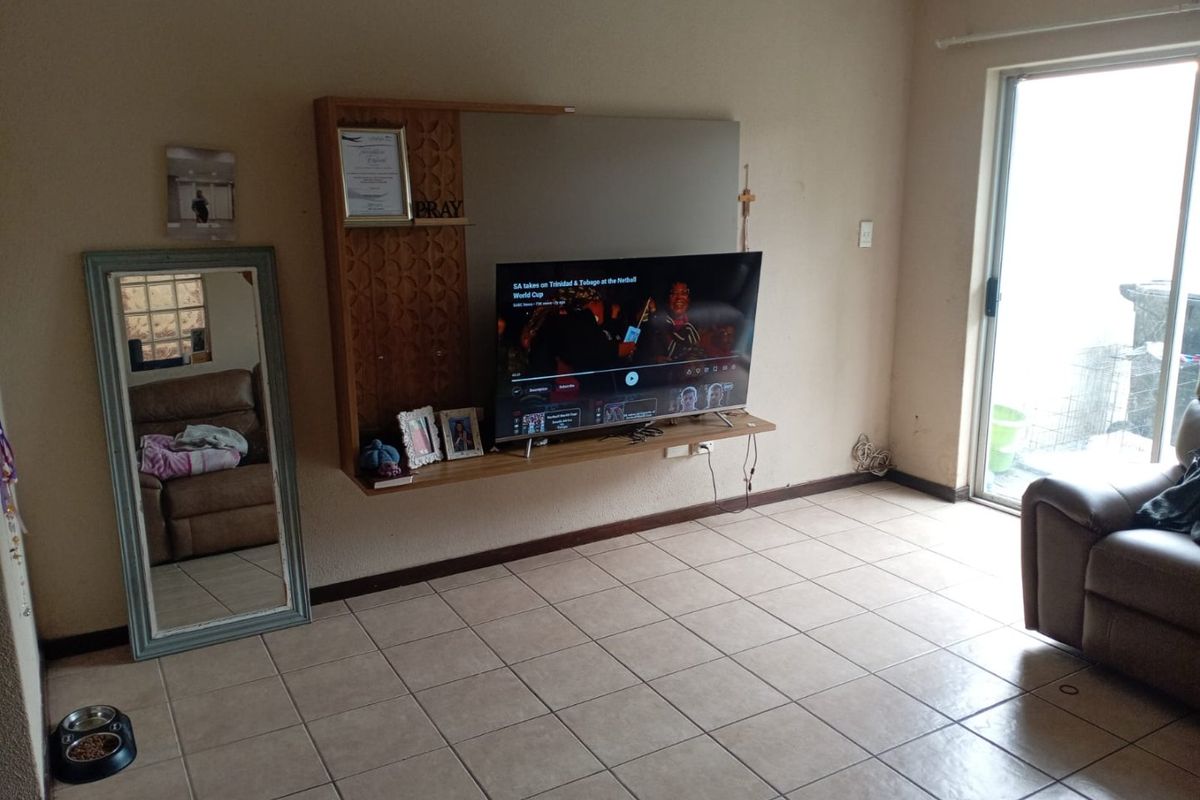 A living room featuring tiled flooring, a wall-mounted entertainment unit, and a sliding glass door providing access to the exterior.