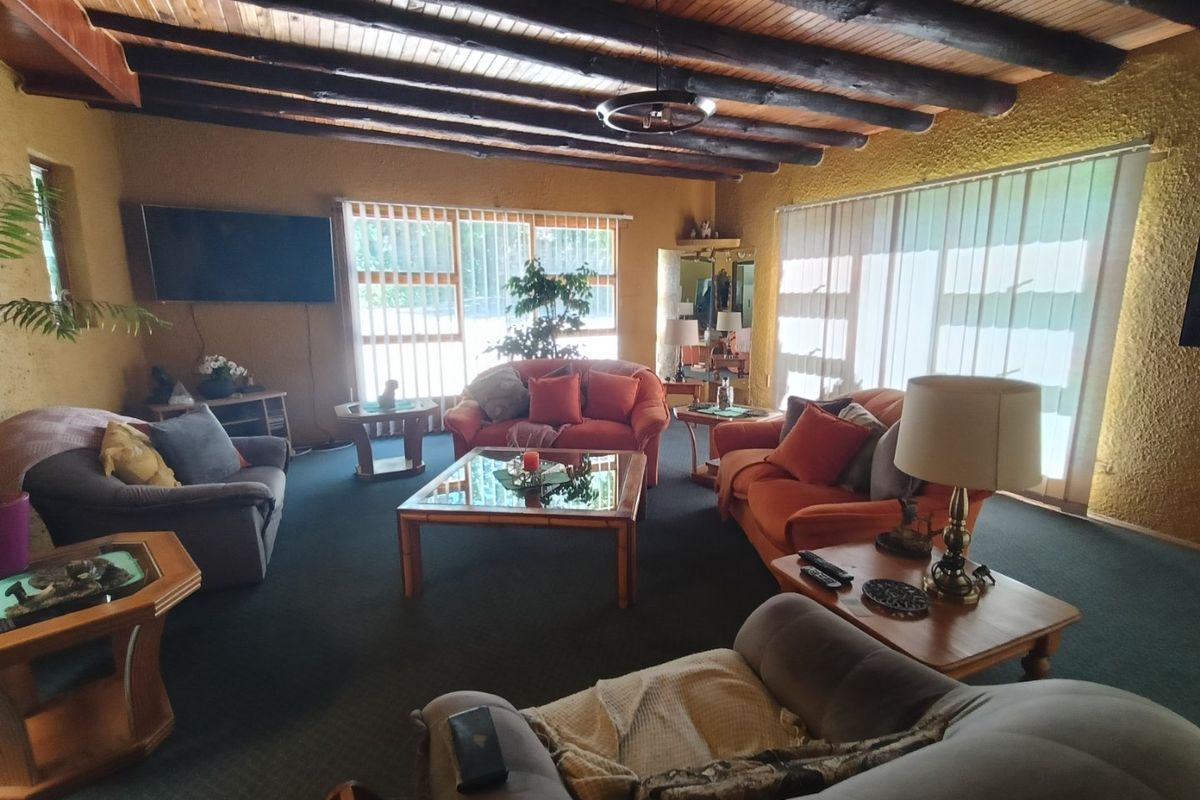 Spacious living room featuring a rustic exposed timber beam ceiling, textured walls, and large windows with vertical blinds providing ample natural light.