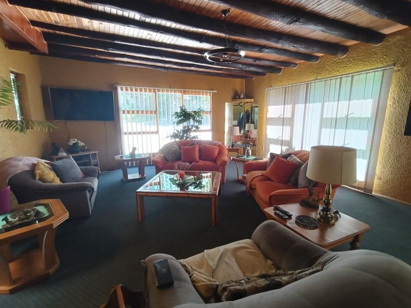 Spacious living room featuring a rustic exposed timber beam ceiling, textured walls, and large windows with vertical blinds providing ample natural light.