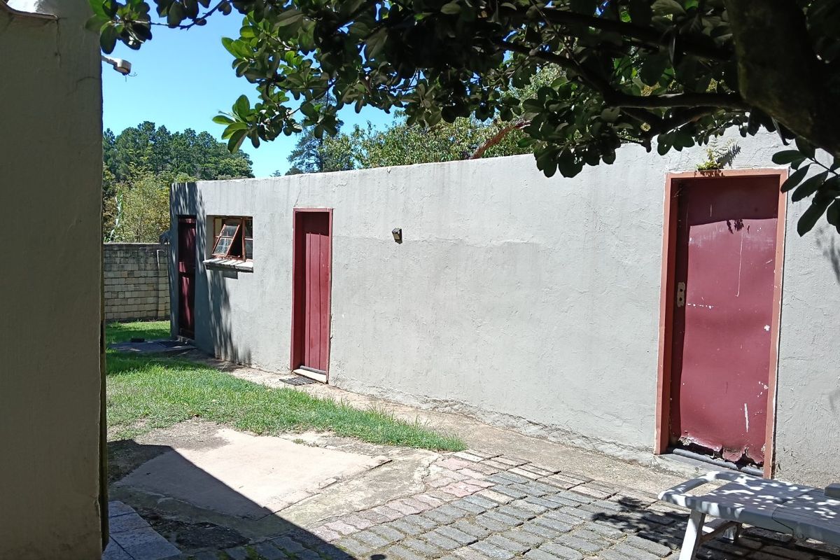 Rear exterior view showing a paved courtyard area with access to multiple external doors and a boundary wall.