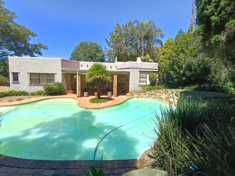 Rear exterior view featuring a swimming pool, stone retaining wall, and a covered patio area with brick pillars.
