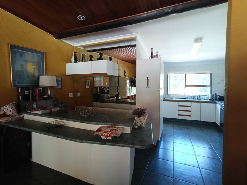 A dated kitchen featuring timber ceilings, tiled flooring, laminate countertops, and a mirrored splashback, offering significant potential for a modern renovation.