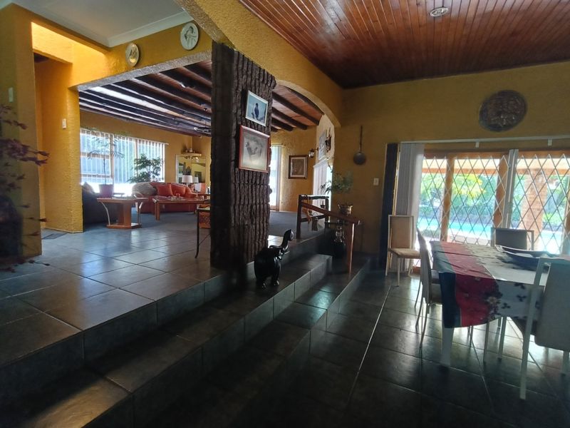Spacious open-plan living and dining area featuring a split-level layout, exposed timber ceilings, and large sliding doors leading to the outdoor pool area.