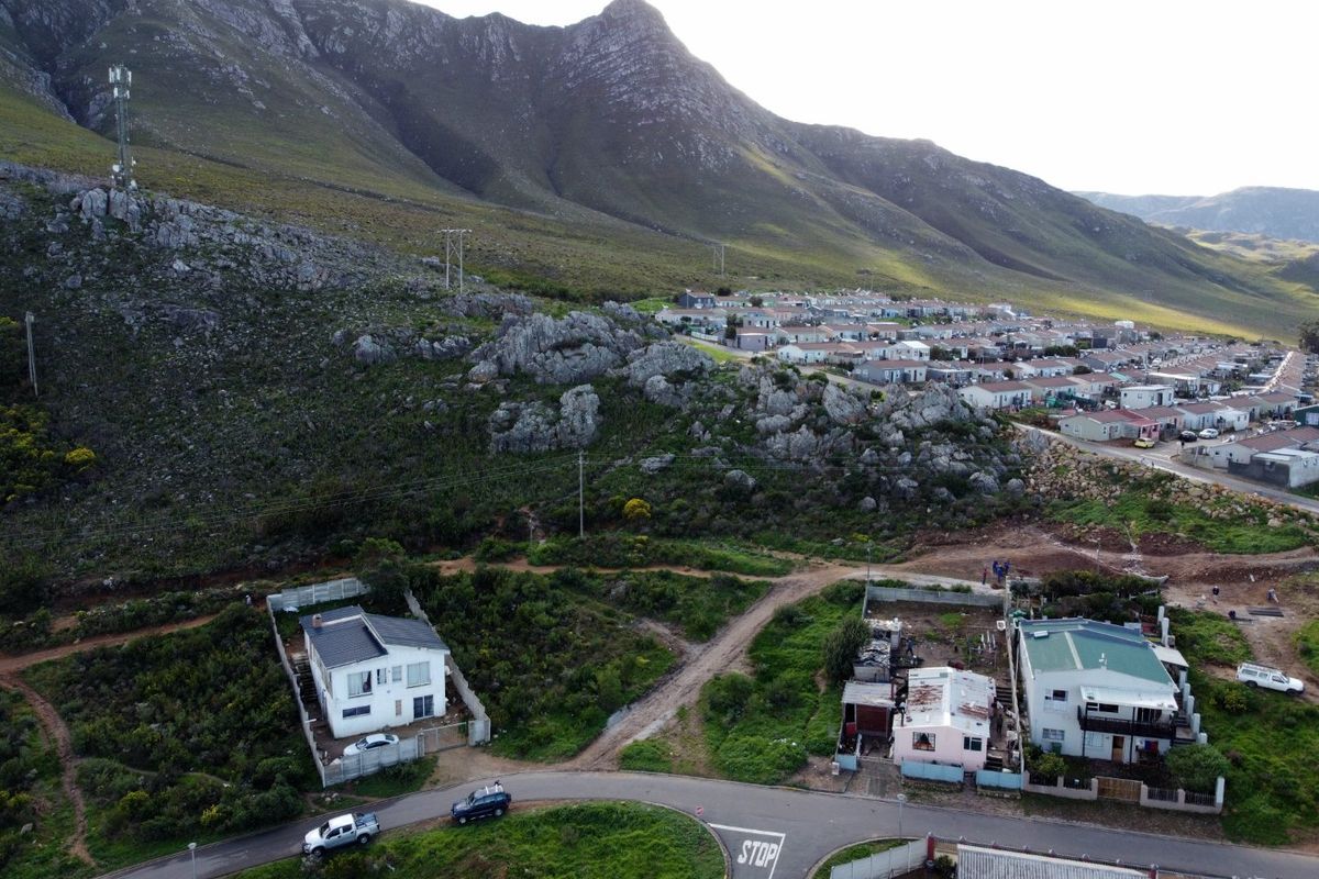 Aerial view of a residential area featuring vacant land plots situated against a prominent mountain backdrop with established street access.