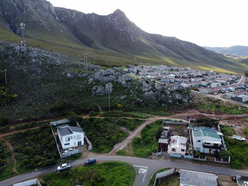 Aerial view of a residential area featuring vacant land plots situated against a prominent mountain backdrop with established street access.