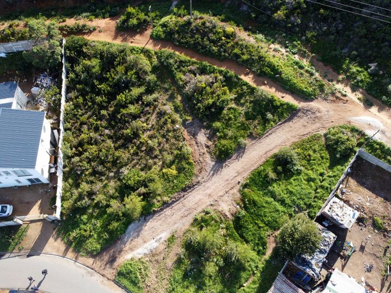 Aerial view of a vacant residential plot featuring natural vegetation, dirt access paths, and surrounding boundary fencing.