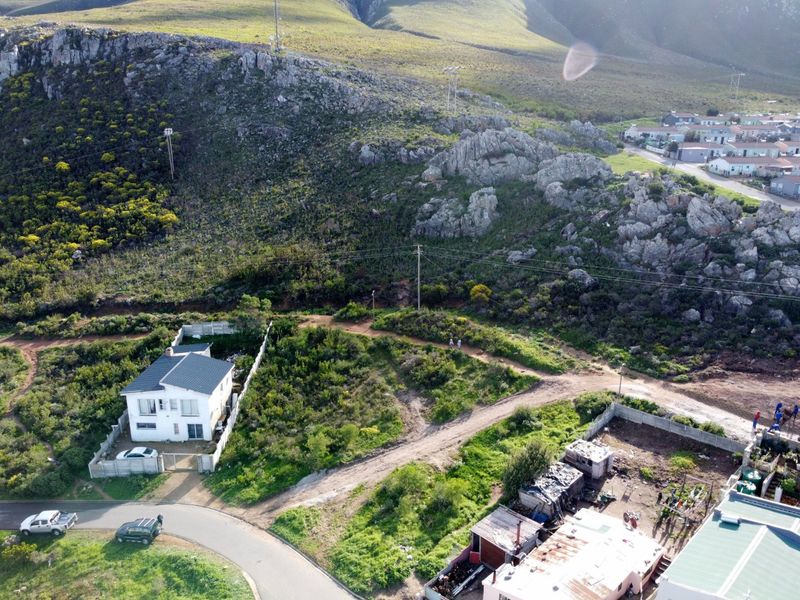 Aerial view of a residential property situated at the base of a rocky mountain slope with surrounding natural landscape and access roads.