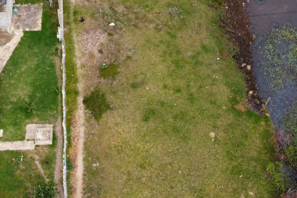 Aerial view of a vacant residential plot featuring grass coverage, boundary fencing, and adjacent water feature.