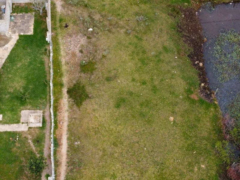 Aerial view of a vacant residential plot featuring grass coverage, boundary fencing, and adjacent water feature.