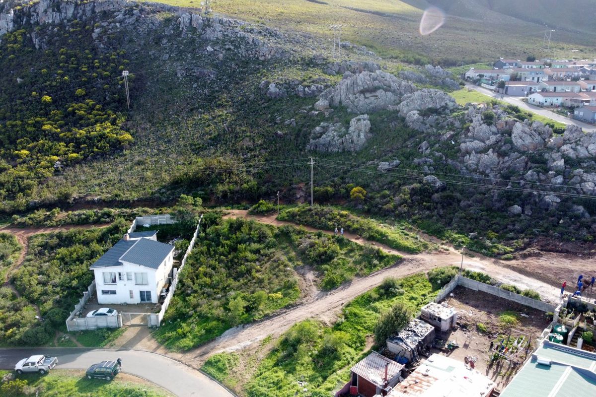 Aerial view of a residential property situated at the base of a rocky mountain slope with surrounding natural landscape and access roads.