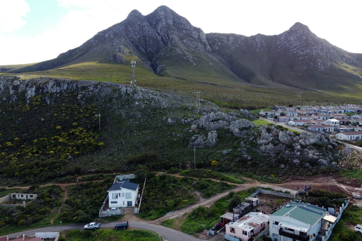 Aerial view of a residential area situated at the base of a large mountain, featuring local infrastructure and surrounding landscape.