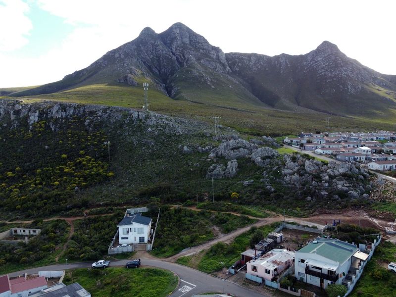 Aerial view of a residential area situated at the base of a large mountain, featuring local infrastructure and surrounding landscape.