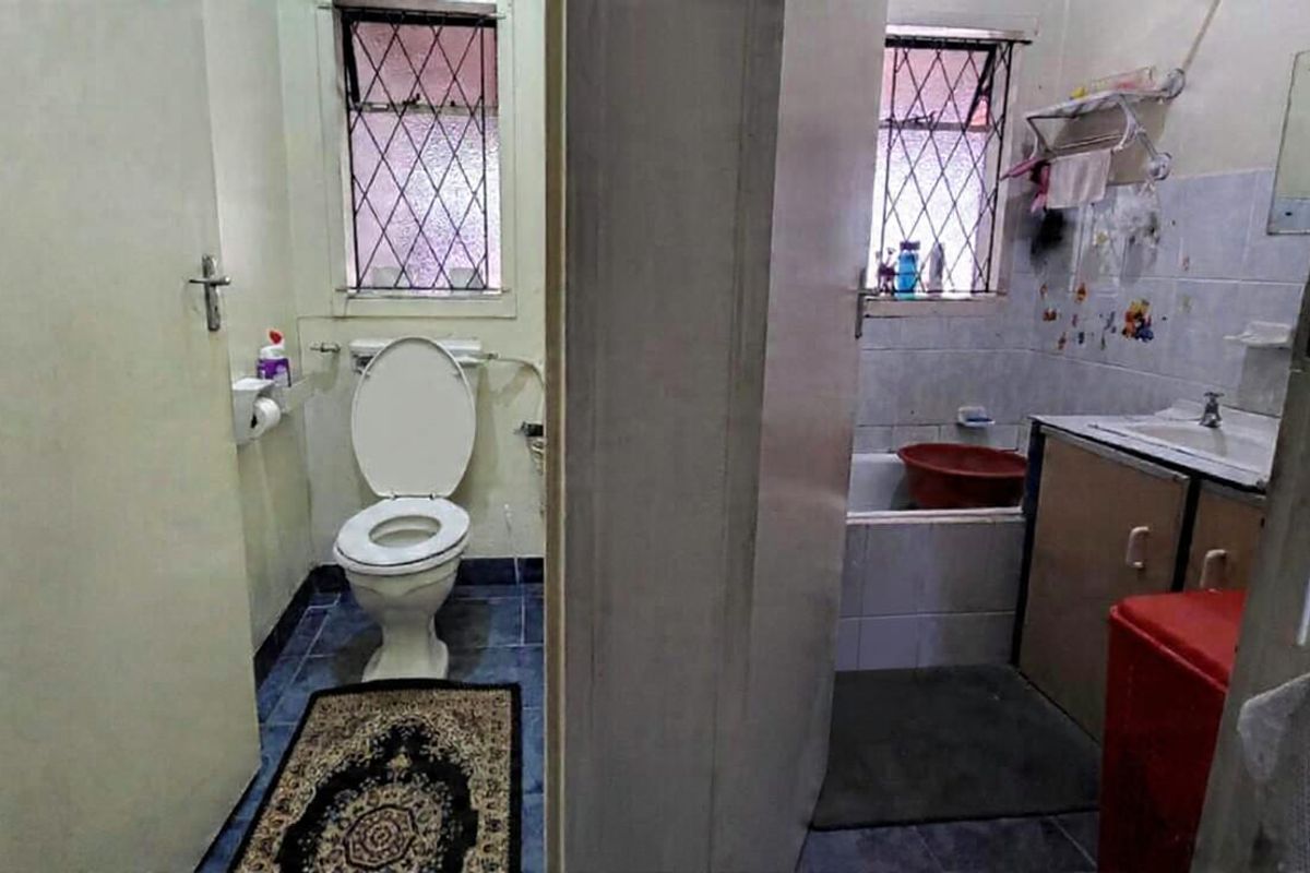 A dated bathroom featuring a separate toilet area, bathtub, and vanity with security bars on the windows.