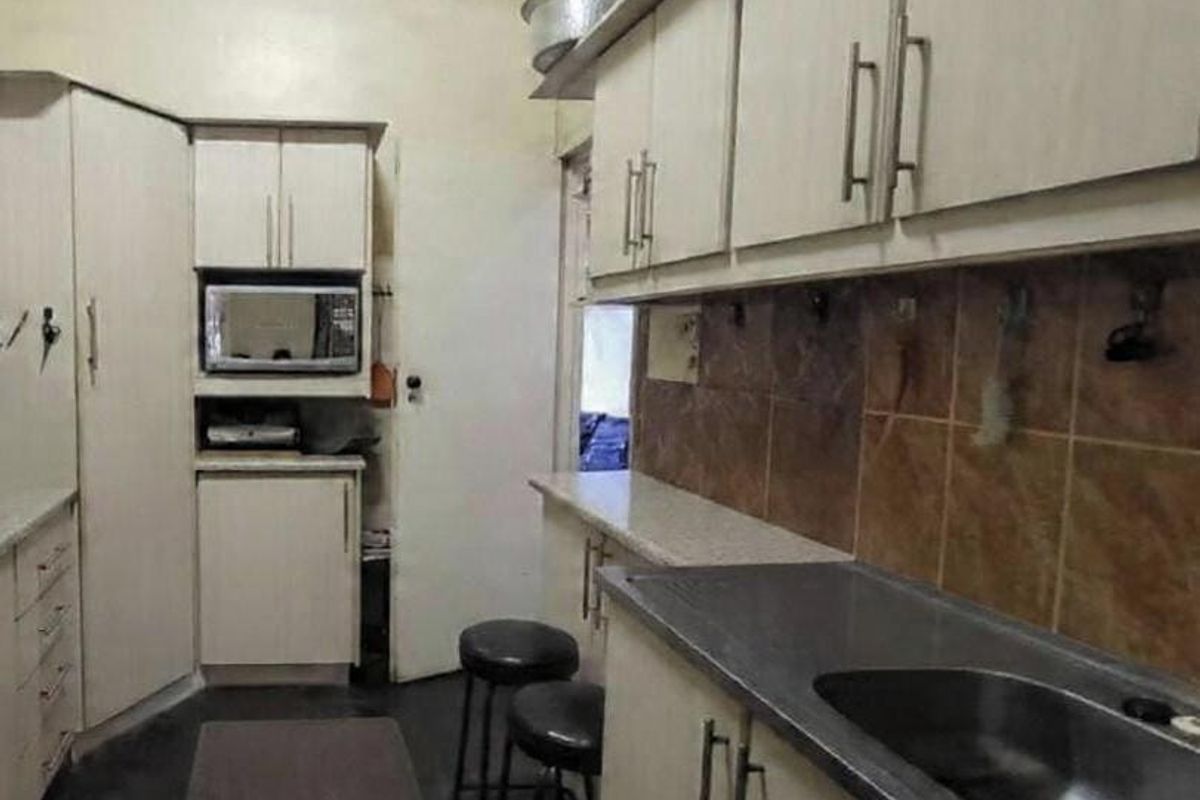 A functional kitchen featuring built-in cabinetry, a stainless steel sink, and a tiled backsplash, offering potential for modernization and cosmetic updates.