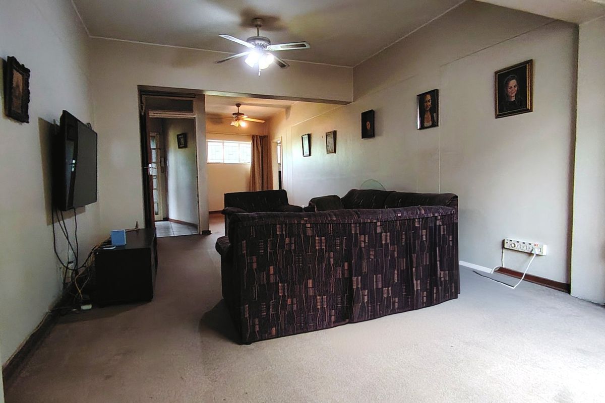 A spacious living room featuring carpeted flooring and ceiling fans, offering a neutral canvas for potential interior updates and modernization.