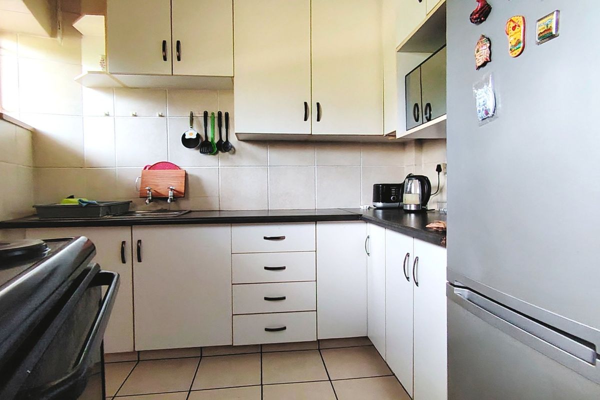 A functional kitchen featuring white cabinetry, dark laminate countertops, tiled backsplash, and tiled flooring, providing a clean and practical workspace.